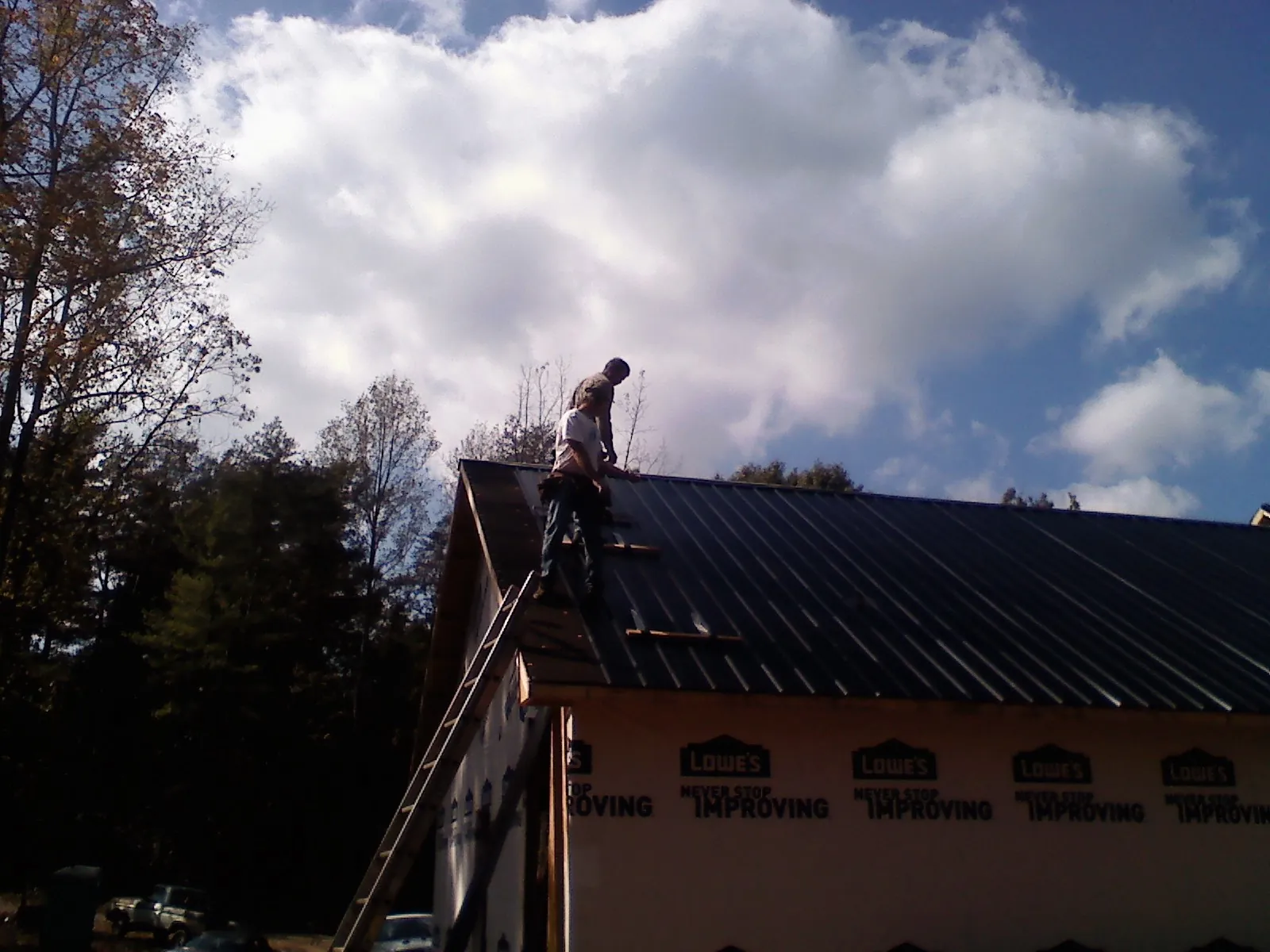 Roofer fastening dark metal panels high against a cloudy sky in Duncan